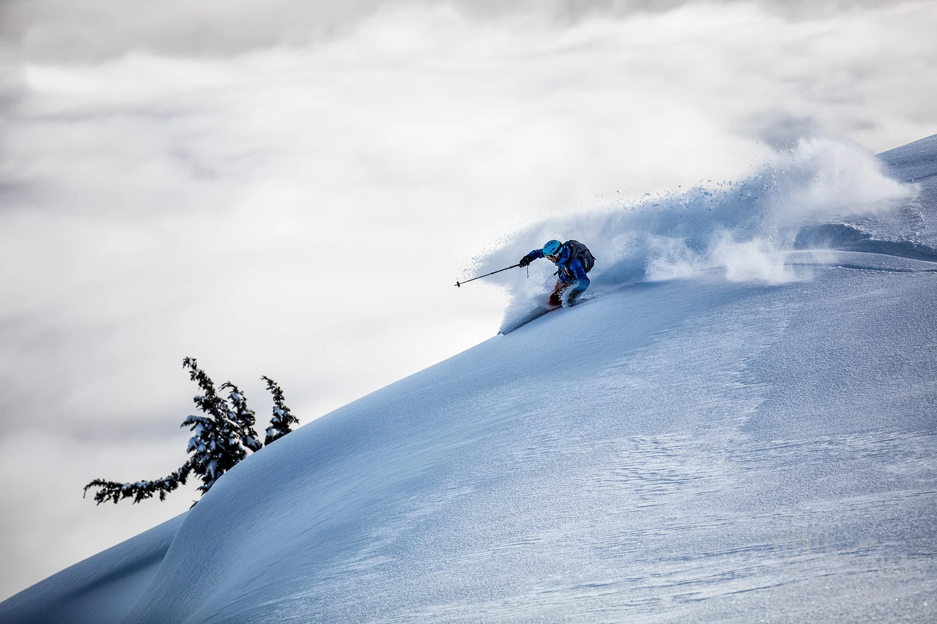 Skieur traçant une courbe dans la poudreuse sur une pente raide au-dessus des nuages
