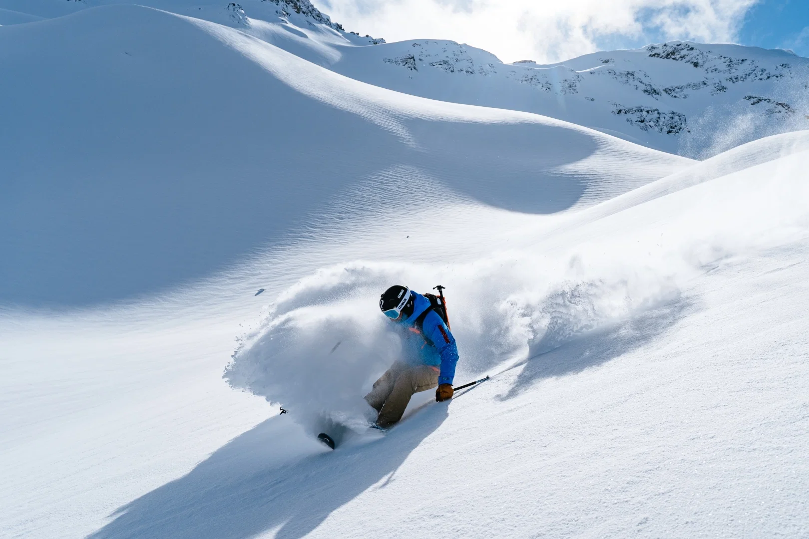 Skieur soulevant un panache de poudreuse dans une combe ensoleillée