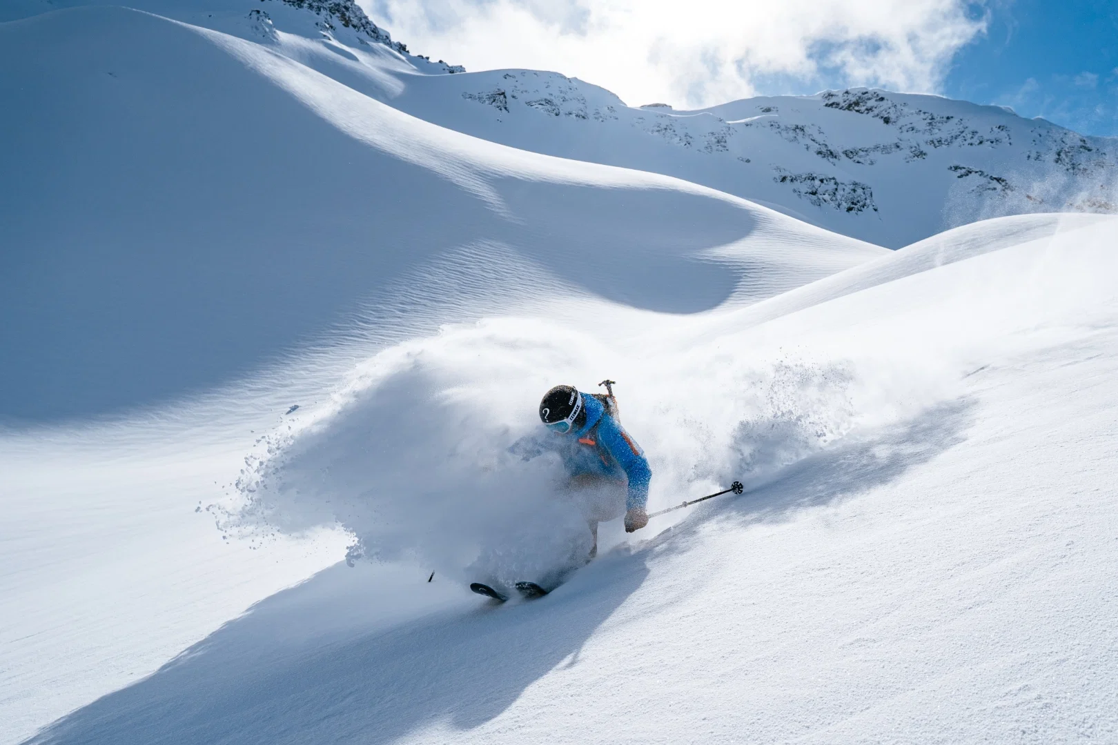 Skieur en veste bleue soulevant la poudreuse en haute montagne ensoleillée