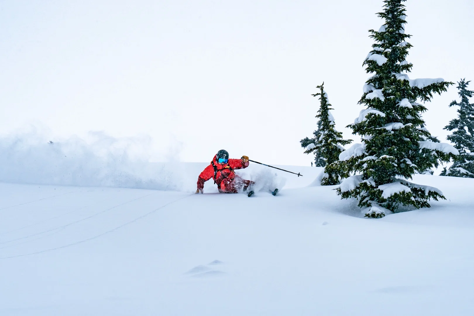 Skieur en veste rouge dans la poudreuse profonde à côté de sapins enneigés